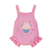 Pink knitted baby romper overalls with cupcake embroidery, frilly hem, and buttoned leg openings.