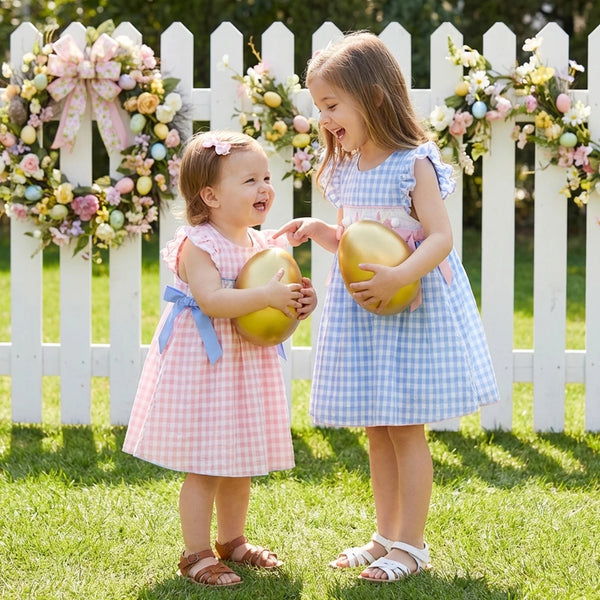 Two girls wear Frilly Bunnies Embroidered Dresses in Palm Beach Pink and Boca Blue, holding golden eggs.
