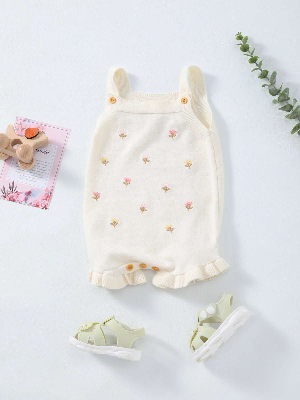 Cream knit baby romper with crocheted flowers, button straps, and frilly hem.