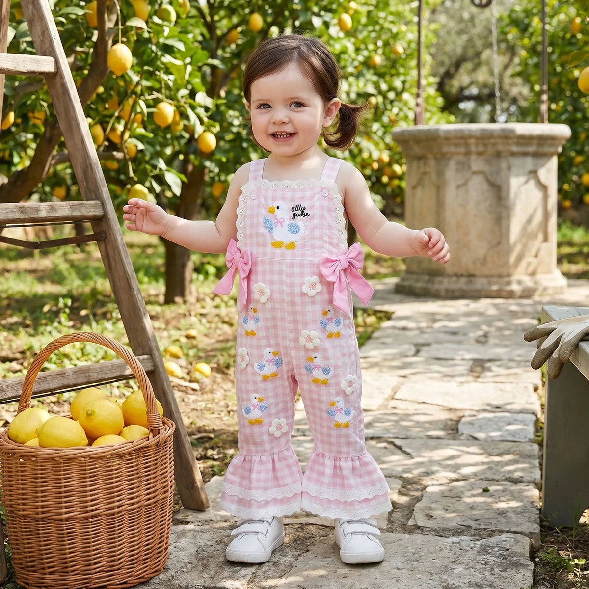 Child in a pink floral dress with bird designs standing in an orchard with lemons.