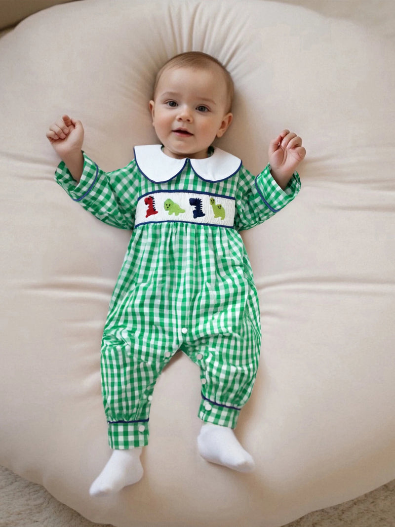 Cute infant lying on a soft cushion, dressed in the 'Dino-Might!' Long Sleeve Peter Pan Collar Check Romper with a green checked design and charming dinosaur embroidery.