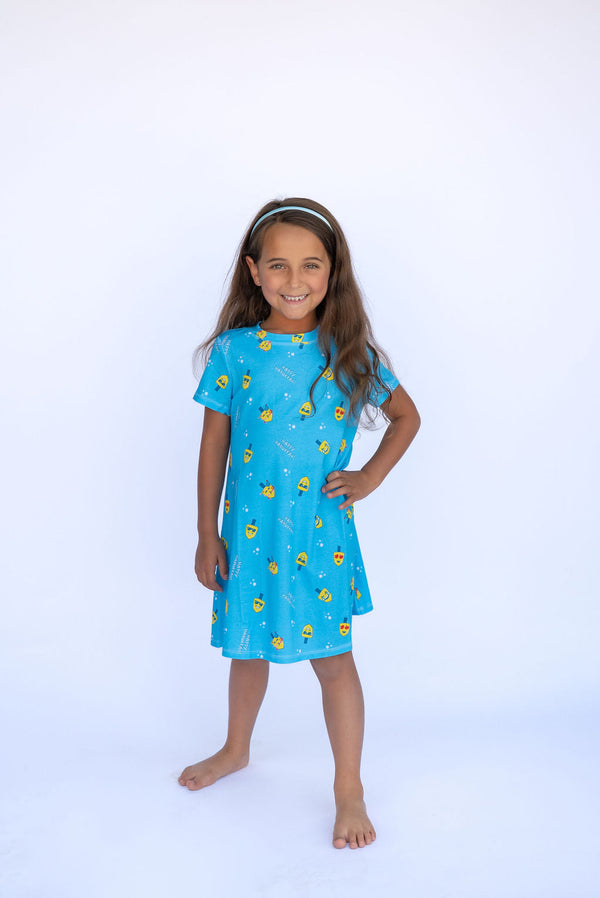 Girl in Lovin' Dreidels blue A-Line dress for 2-9 years, festive dreidel print, smiling.