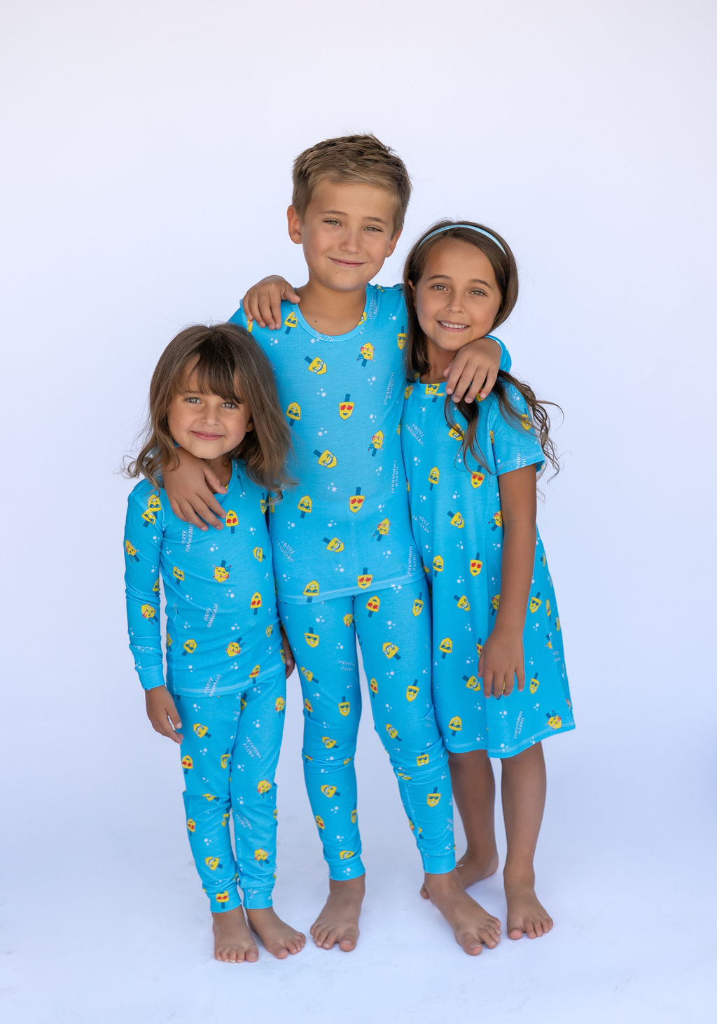 Three kids in blue Lovin' Dreidels outfits with yellow dreidel print, A-Line dress style for 2-9 years.