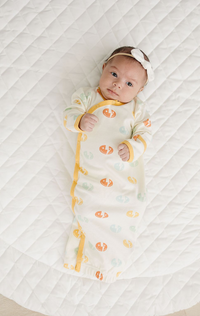 Baby wearing GOTS certified organic cotton sleep gown with smiley bolt print and yellow trim on quilted white blanket.