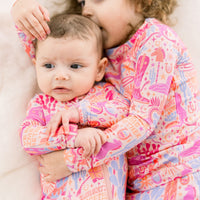 Two children cuddle in The Second-Skin 2-Piece Long Sleeve Pajama Saddle Up in pastel pink cowgirl print.