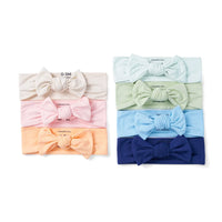 Stacked display of seven pastel and solid color baby bow headbands including cream, pink, mint, and navy