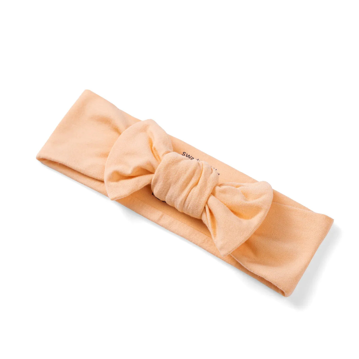 Diagonal view of peach stretchy newborn hair accessory highlighting twisted fabric bow construction