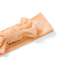 Macro shot of ribbed knit texture on peach wide knit baby headband with visible snug-fitting instruction