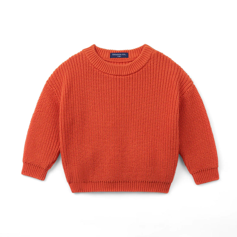 Rust-orange chunky knit baby sweater with ribbed collar and navy Swaddle AN label on white background