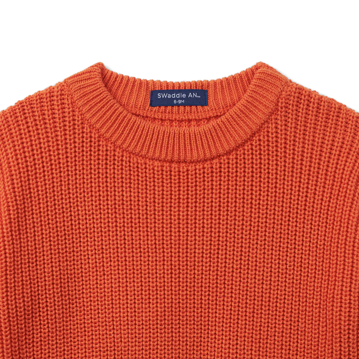 Close-up of orange knit baby sweater neckline showing tight vertical stitch texture and navy size tag
