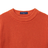 Close-up of orange knit baby sweater neckline showing tight vertical stitch texture and navy size tag