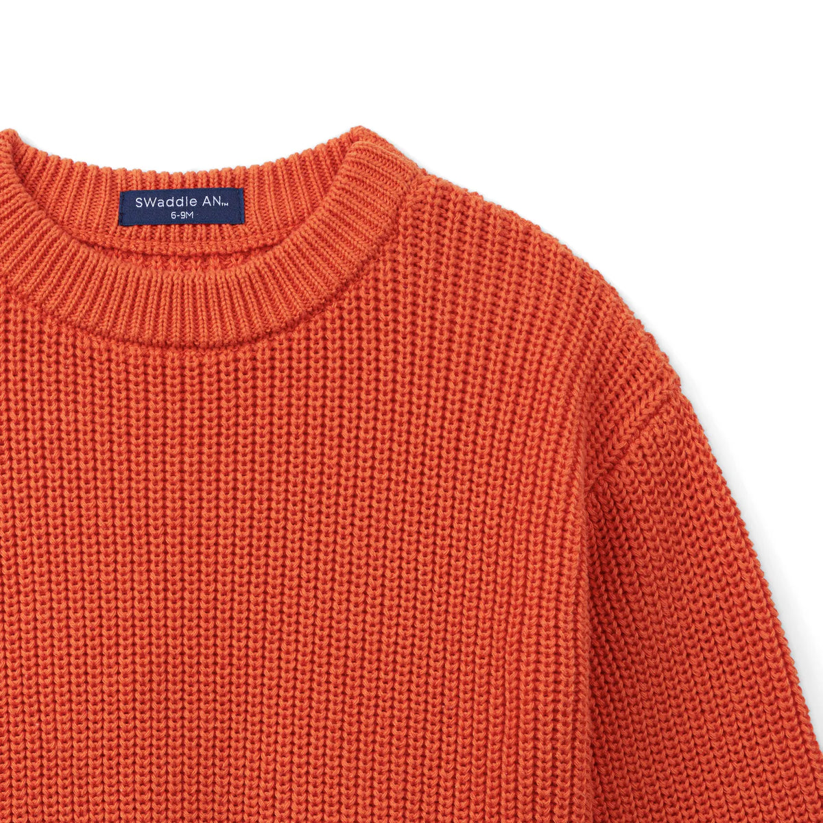 Angled view of rust-orange baby sweater shoulder seam and ribbed crew neck collar detail