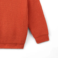 Macro shot of ribbed sleeve cuff and hem on rust-orange baby sweater showing durable fabric weave