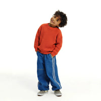 Smiling toddler wearing rust-orange cotton crewneck sweater, blue jeans, and checkerboard slip-on shoes