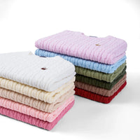 Stacks of folded baby sweaters in multiple colors including lilac, blue, green, and red with embroidered logos
