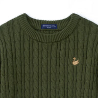Close-up of navy SWaddle AN size tag and gold swan logo embroidered on forest green cable knit fabric texture