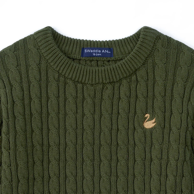 Close-up of navy SWaddle AN size tag and gold swan logo embroidered on forest green cable knit fabric texture