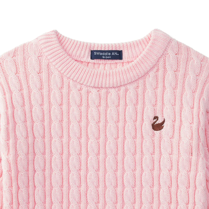 Close-up of pink baby sweater showing navy brand tag, ribbed neckline, and textured vertical cable knit pattern