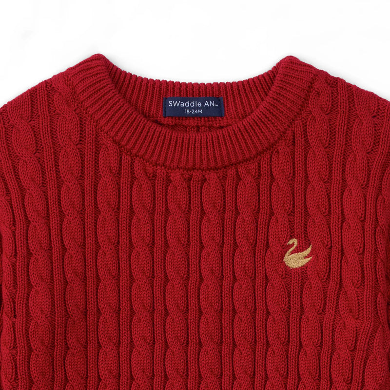 Close up of red cotton cable knit texture, navy size label, and gold embroidered swan detail