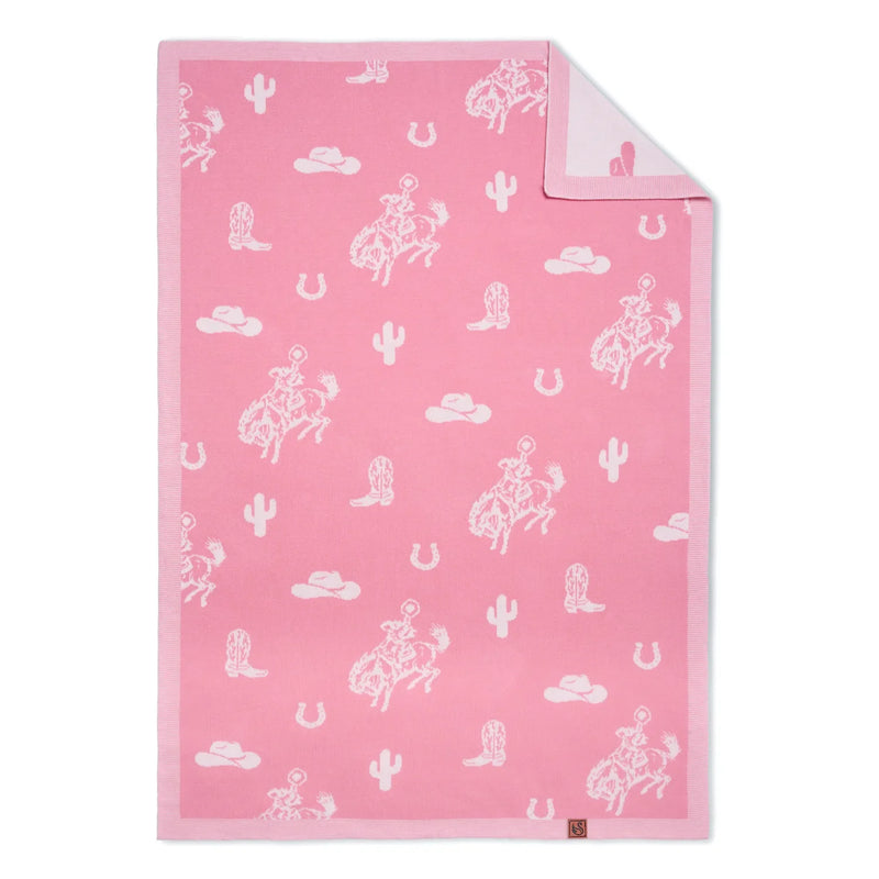 Pink jacquard knit baby blanket flat lay showing western motifs like cowgirls and cacti, with corner folded to reveal lighter