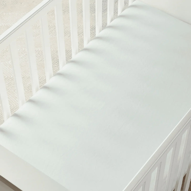Light mint green fitted crib sheet stretched taut over a white crib mattress with soft shadows from vertical slats