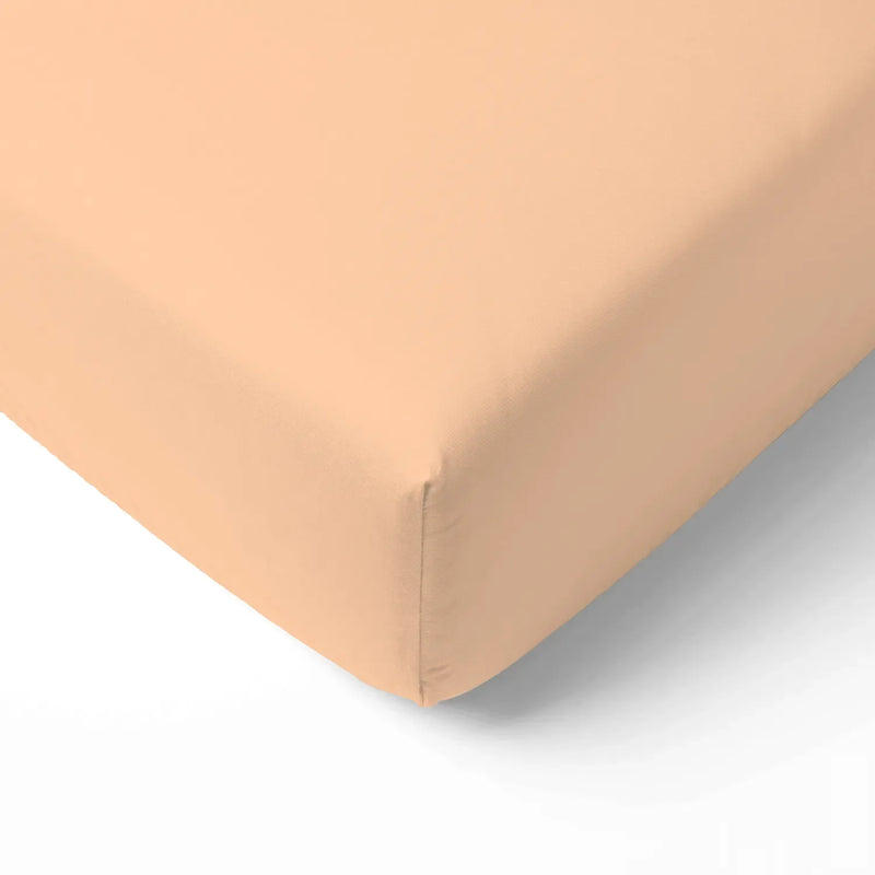 Close-up of peach fuzz bamboo crib sheet corner with deep elastic pocket fitting snugly over mattress edge