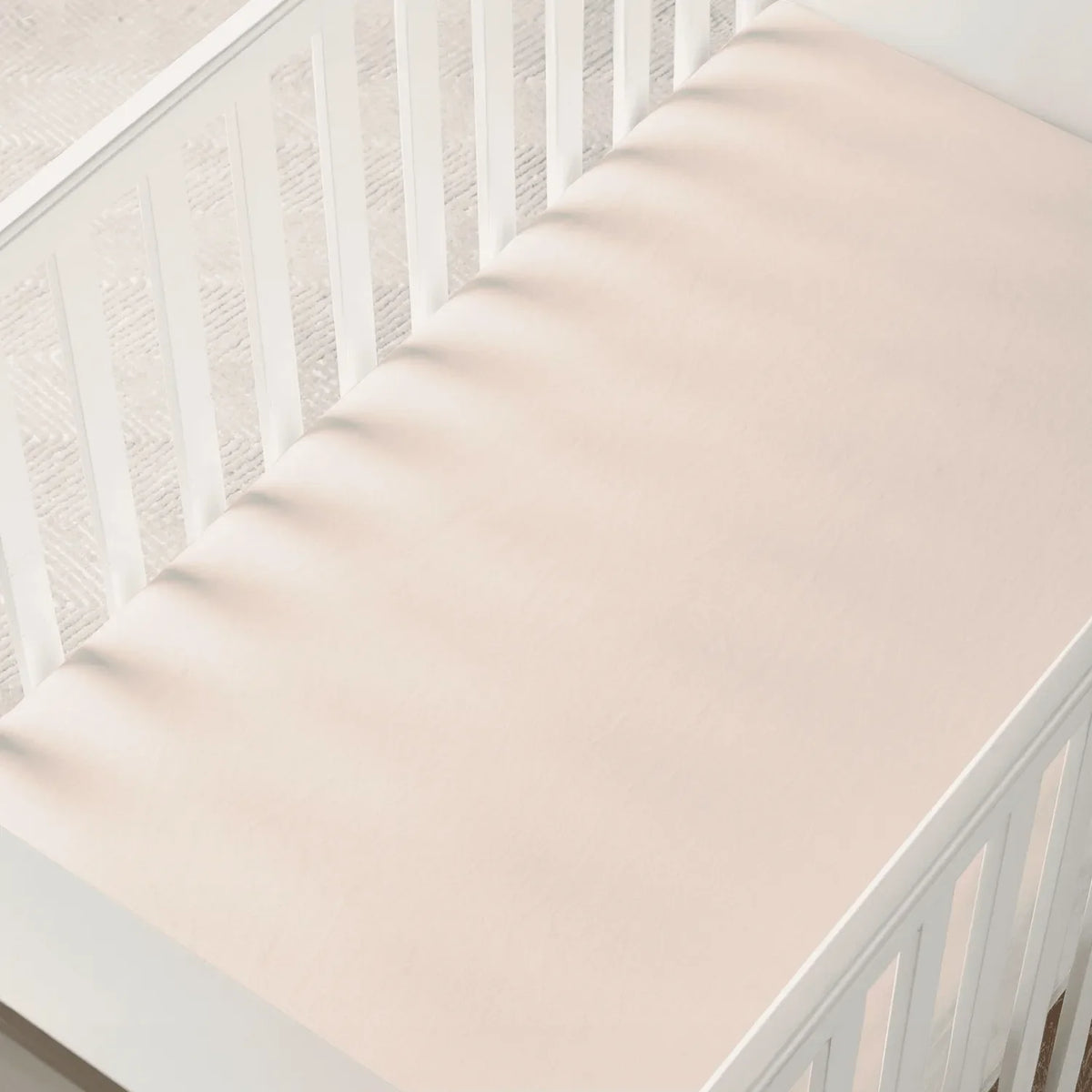 Overhead view of sand bamboo crib sheet in white crib with soft shadows from slats