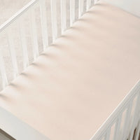 Overhead view of sand bamboo crib sheet in white crib with soft shadows from slats