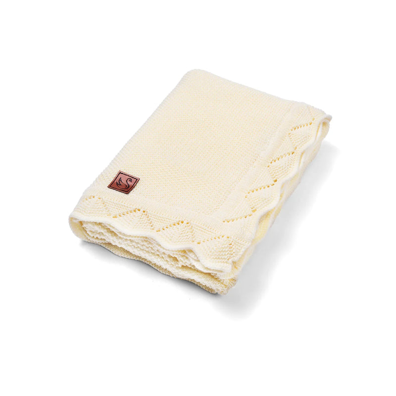 Folded cream knit baby blanket with delicate lace border and brown leather swan logo patch