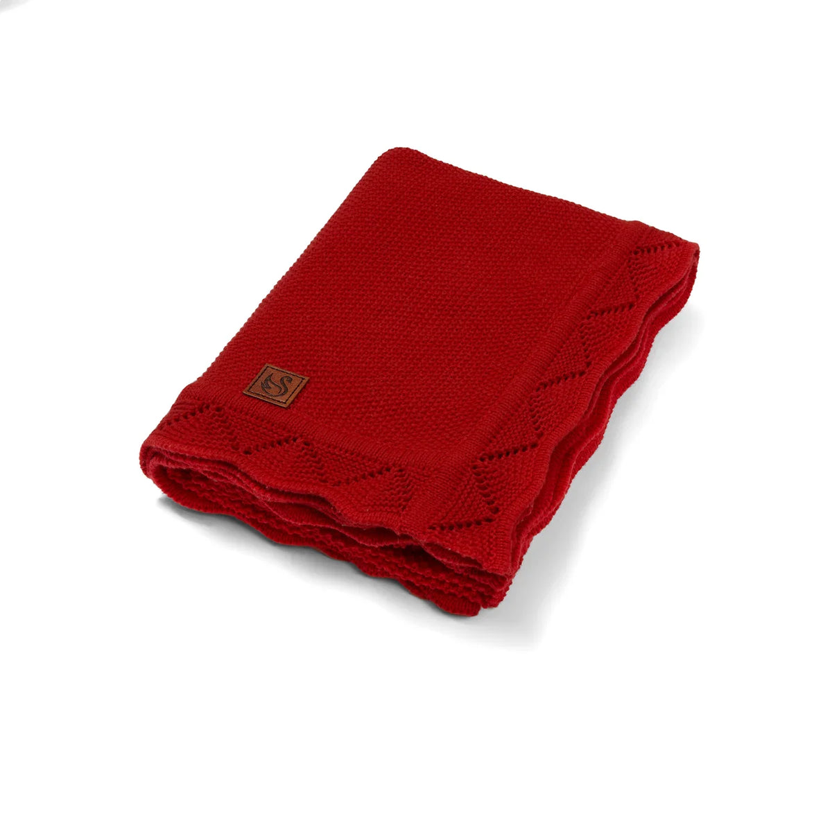 Folded red knit baby blanket with lace border and brown logo patch on white background