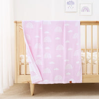 Rainbow lilac knit blanket draped over natural wood crib rail in bright nursery with cream bumper and artwork