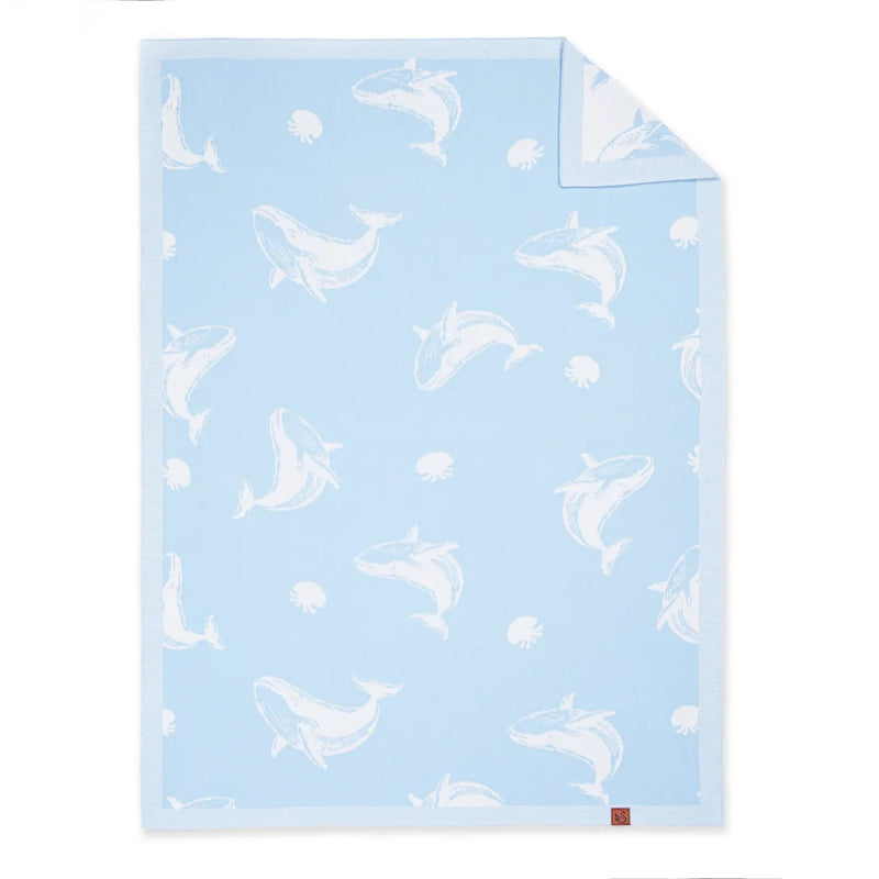 Light blue whale jacquard knit baby blanket flat lay with white whales, folded corner revealing white reverse and brown tag