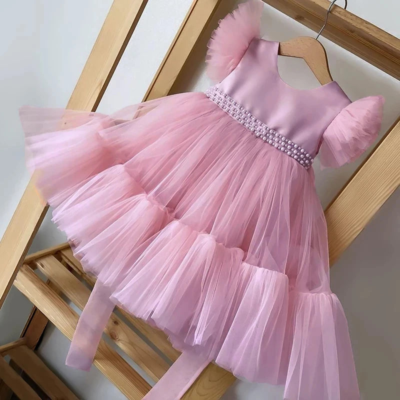Pink 'Pretty In Tulle' Girls Tulle Party Dress hanging on a wooden hanger, showcasing its beaded waist and flared skirt with tulle layers.