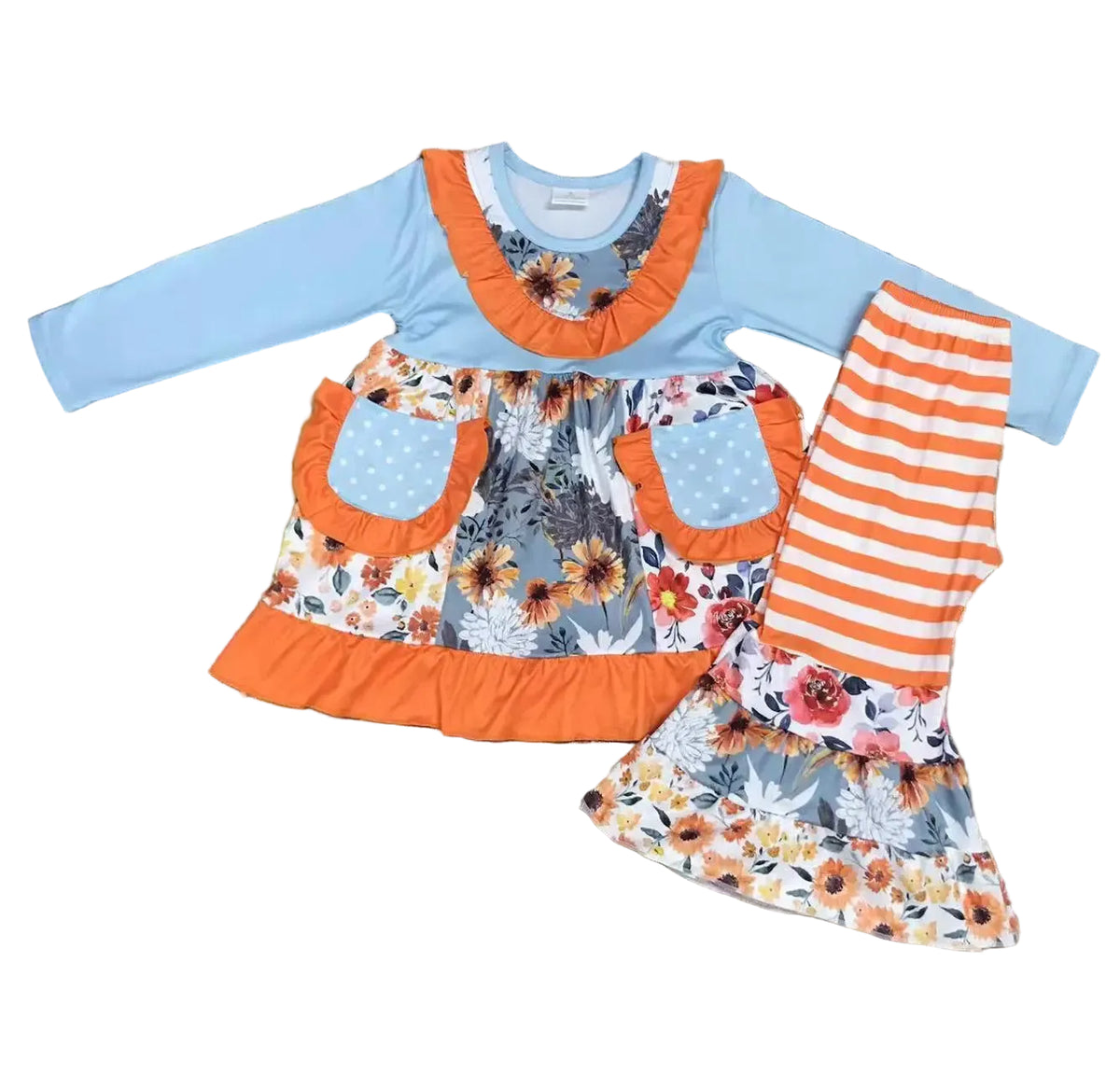 A children's two-piece outfit laid flat on a dark wood floor, featuring a light blue long-sleeve top with orange ruffle trim and a floral apron-style front panel, paired with orange-and-white striped leggings and a matching floral skirt.