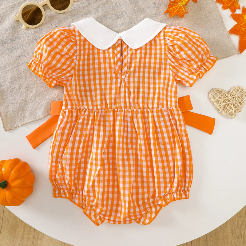 Back view of the Gingham Cutie Baby Pumpkin Romper on a table with autumn leaves, focusing on the cute design.