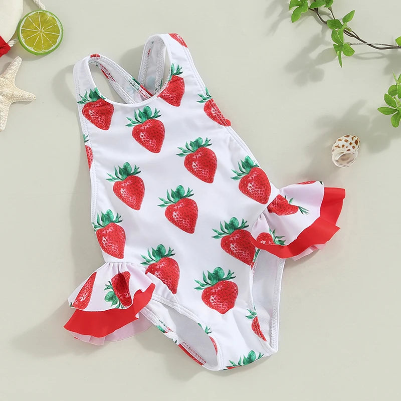 White strawberry-print toddler girl one-piece swimsuit with crisscross back and red frilly side ruffles.