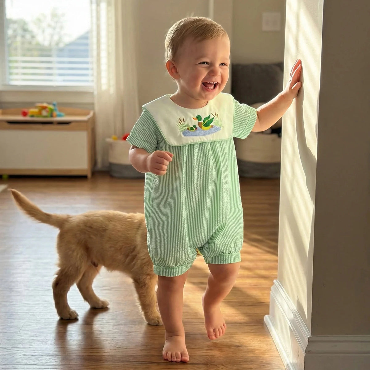 Little Ducky Boys bibbed seersucker romper in green stripes with embroidered mallard ducks, baby at home.
