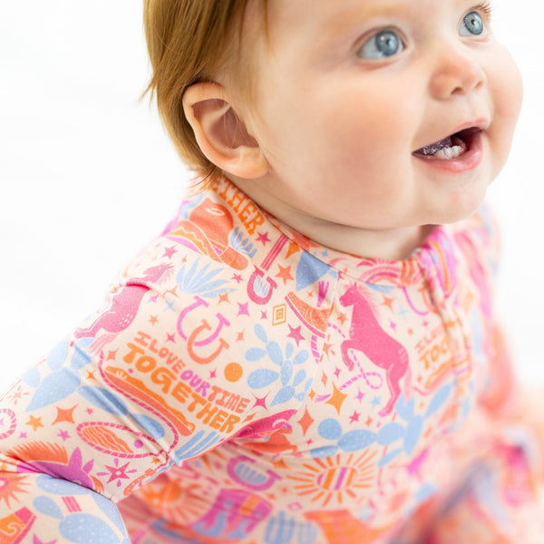 Baby wearing The Second-Skin Convertible Romper Saddle Up in a colorful print