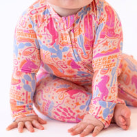 Baby in The Second-Skin Convertible Romper Saddle Up; vibrant pink, orange, blue pattern with zipper front.