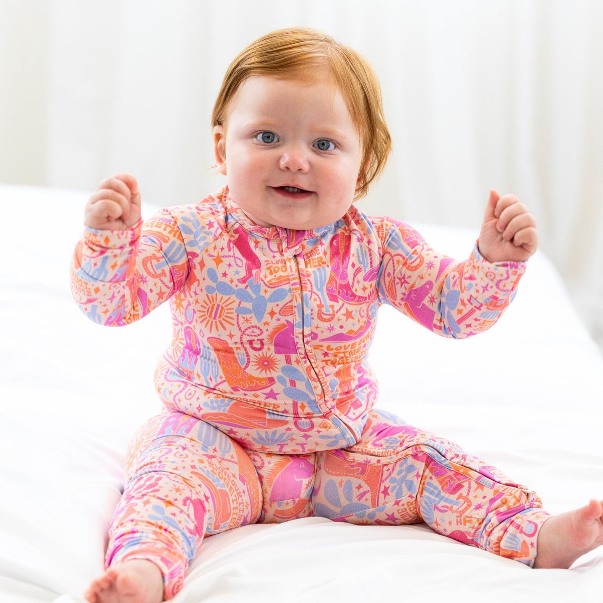 Infant wearing The Second-Skin Convertible Romper | Saddle Up, a colorful zip-front one-piece.