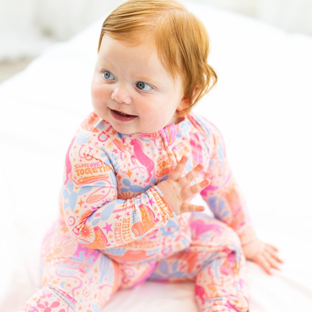 Smiling baby in a colorful printed long-sleeve romper with pink, blue, and orange patterns.