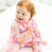 Smiling baby in a colorful printed long-sleeve romper with pink, blue, and orange patterns.