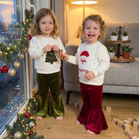 Toddler girls wear Christmas bell bottom sets with Santa and tree print tops and velvet flare pants near holiday window decorations.