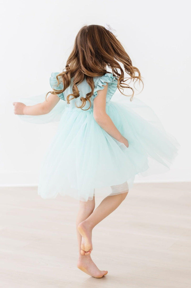 Back view of a girl in a Sage Shimmer Tutu Dress, capturing her twirling and flowing skirt, perfect for a magical moment.
