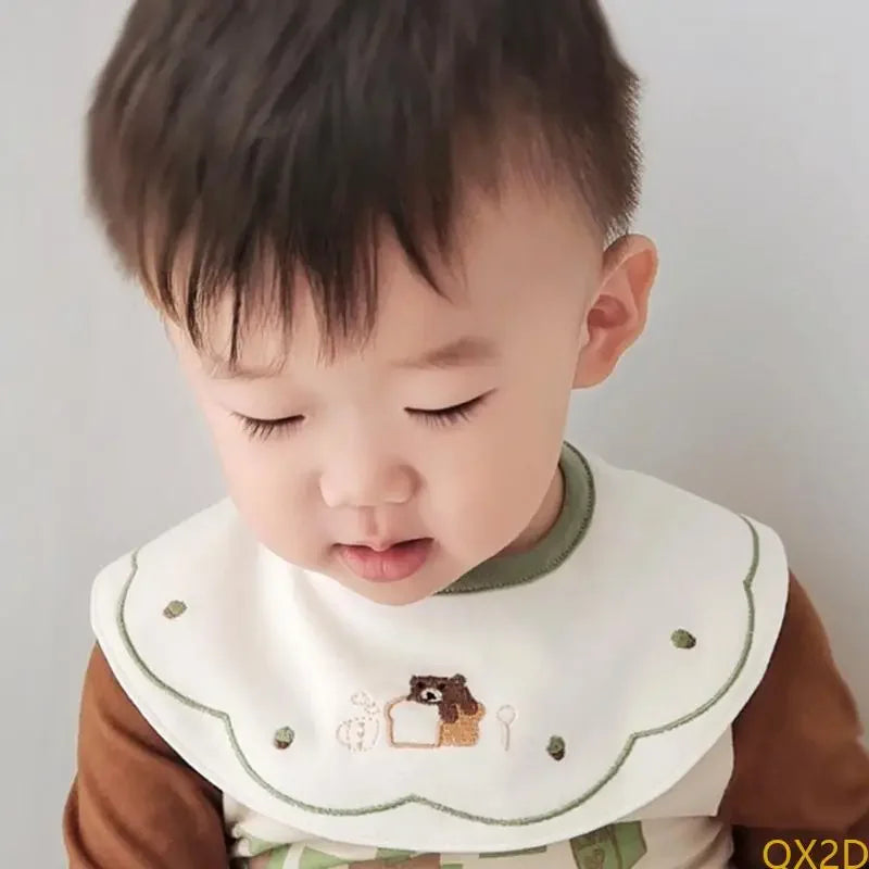 Baby wearing white embroidered waterproof bib with green trim and cute bear design, cotton snap closure meal time accessory.