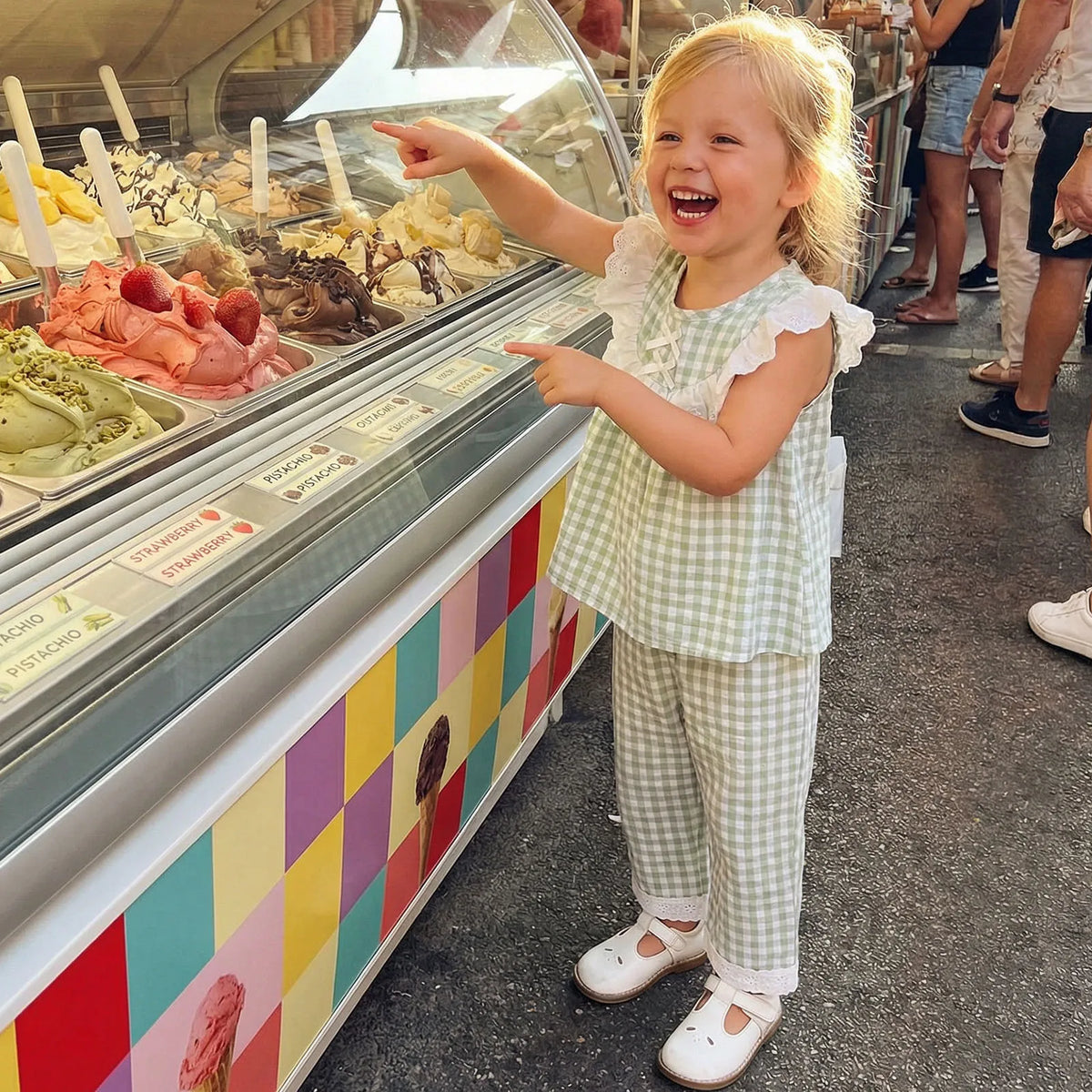 Little girl wearing green gingham eyelet-and-check two-piece pant set with flutter sleeves at an ice cream shop.