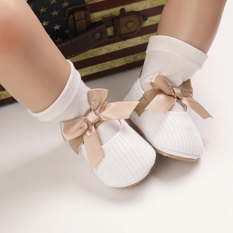 Baby Jane Satin Bow Baby Shoes in white, modeled by a baby, featuring a delightful satin bow.