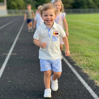 Boy wearing two-piece back-to-school polo set with embroidered pencils and blue checked shorts, running on a track.
