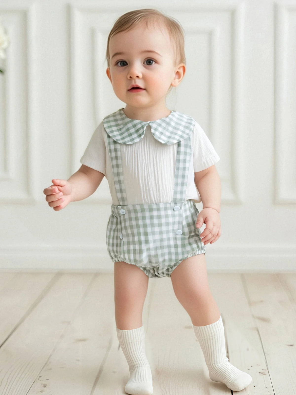 Toddler wearing Carlton Check Romper and Shorts Outfit in mint gingham with white shirt, indoors.