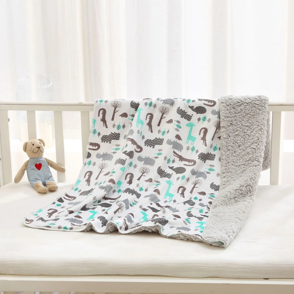Soft children's reversible micro-plush blanket with animal prints in teal and gray on a crib.